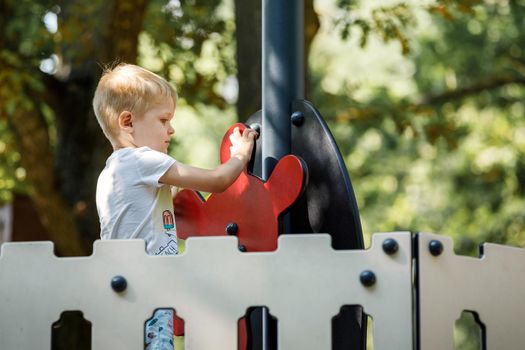 Little boy spinning the helm of a toy ship in a kids playground with confidence.