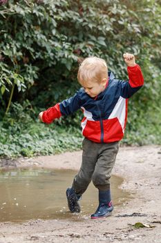 Little boy splashing in a mud puddle, jumping into a puddle.