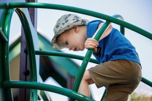 Happy 3 year old boy climbing and playing at outdoor playground in city park.