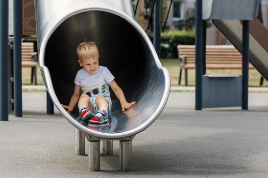 A boy slides down a metal enclosed circular tunnel slide. A child riding the playground slide.