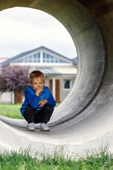 The little boy plays in the yard, he drifts into a large concrete pipe and squats to rest. Vertical photo.