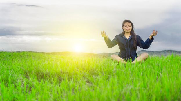 Woman in the field sitting meditating, woman doing yoga in the cool field