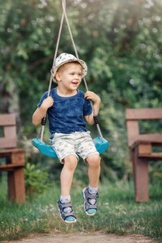 Little boy having fun on a swing on the playground in public park on summer day. Happy child enjoy swinging. Active outdoors leisure for child in city.