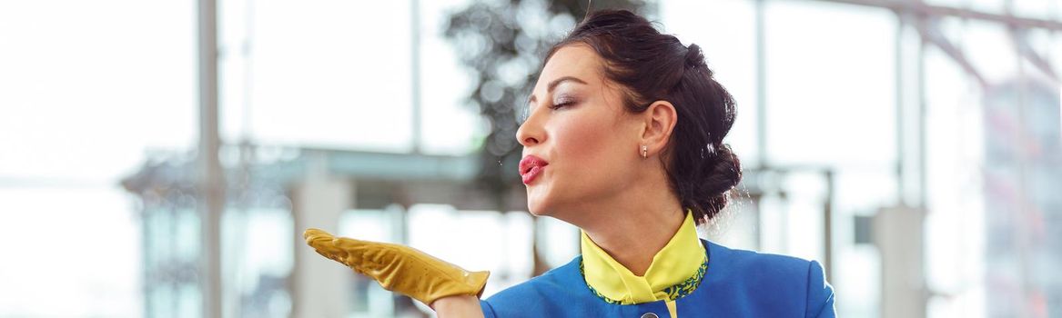 Woman stewardess in aviation air hostess uniform while sending air kiss against blurred background