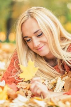 Beautiful young blond hair caucasian woman lies down on leaves at the autumn park