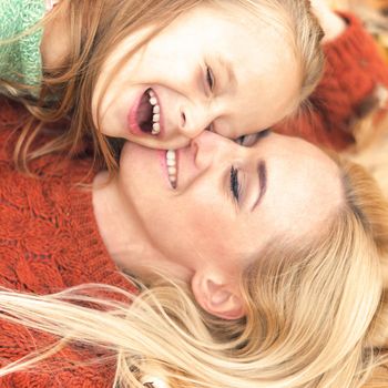 Little girl and young caucasian mom lying down directly above looking at camera on autumn leaves