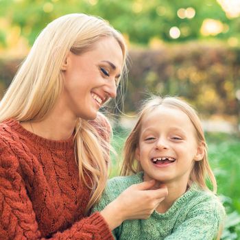 Beautiful young caucasian mother and little daughter smiling together on the green grass in the Autumn Park