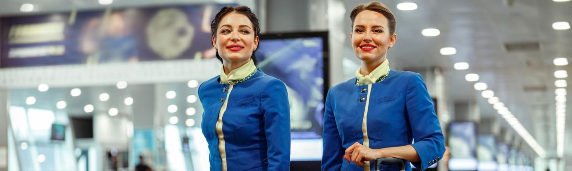 Smiling female flight attendants in aviation air hostess uniform carrying travel bags at airport
