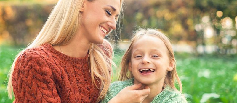 Beautiful young caucasian mother and little daughter smiling together on the green grass in the Autumn Park