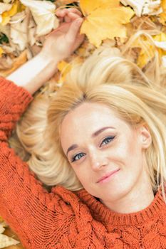 Beautiful young caucasian woman lying down on yellow leaves looking at camera in Autumn Park