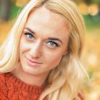 Portrait of beautiful young blond hair caucasian woman looking at camera at the Autumn Park