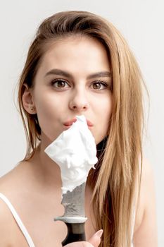 Portrait of young caucasian woman holding knife with shaving foam in front of her face on white background