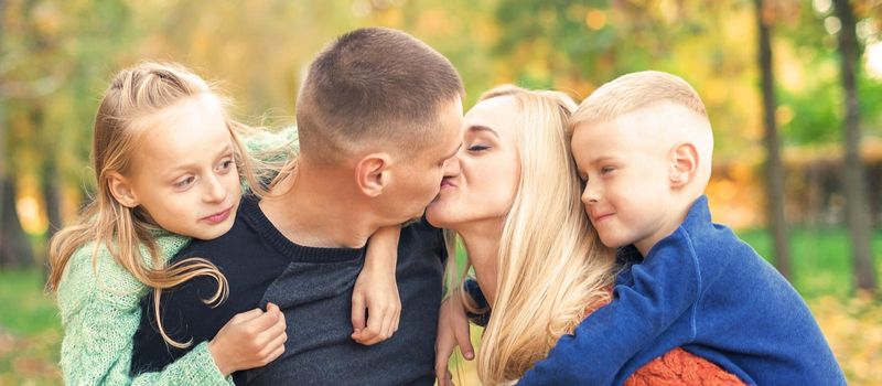 Portrait of young family playing in autumn park. Parents kissing and resting with children in the autumn park