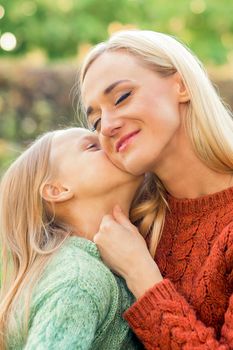Cute daughter kisses her young mother while sitting at the park