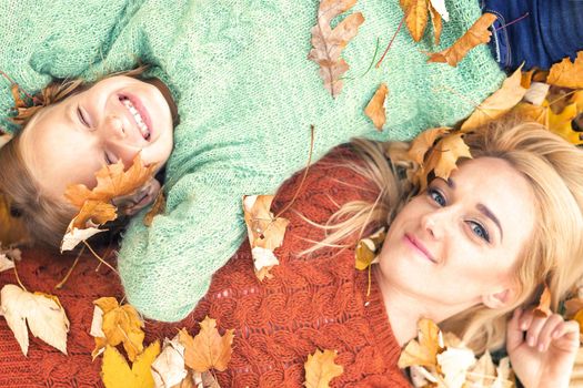 Little girl and young caucasian mom lying down directly above looking at camera on autumn leaves