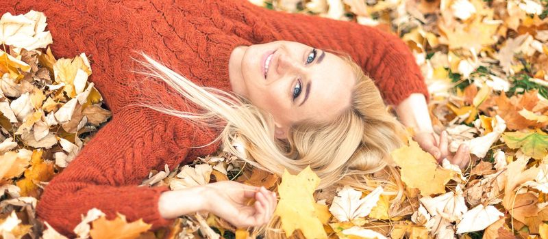 Beautiful young caucasian woman lying down on yellow leaves looking at camera in Autumn Park