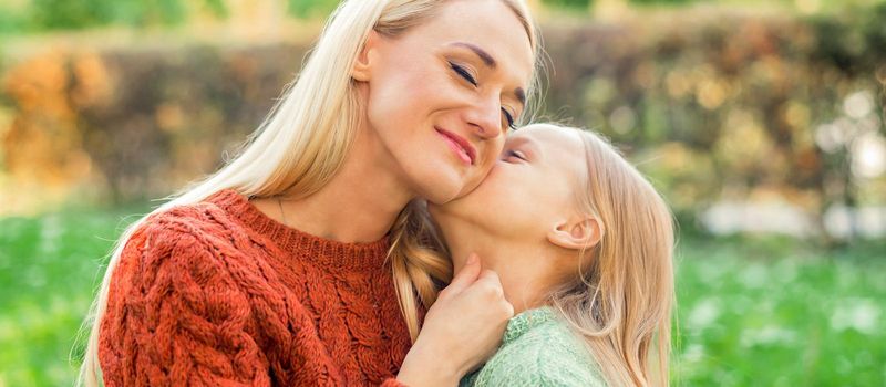 Cute daughter kisses her young mother while sitting at the park