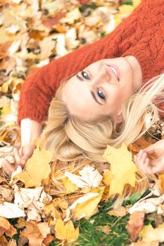 Beautiful young caucasian woman lying down on yellow leaves looking at camera in Autumn Park