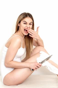 Beautiful young caucasian woman shaves her legs with a knife on a white background