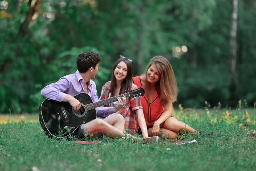 group of students with a guitar relax sitting on the grass in the city Park.