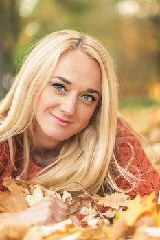 Beautiful young blond hair caucasian woman lies down on leaves at the autumn park