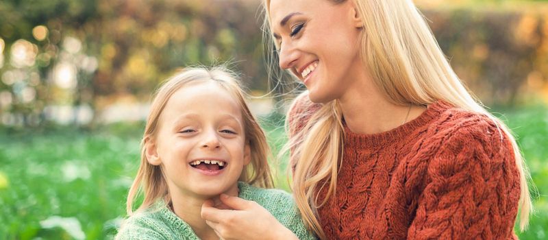 Beautiful young caucasian mother and little daughter smiling together on the green grass in the Autumn Park