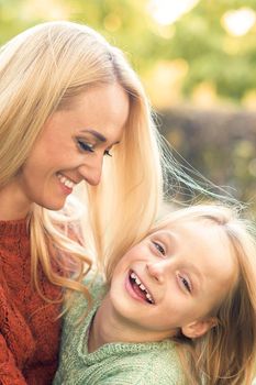 Beautiful young caucasian mother and little daughter smiling together on the green grass in the Autumn Park