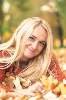 Beautiful young blond hair caucasian woman lies down on leaves at the autumn park