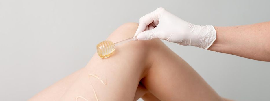 Wax on honey stick flowing down on female leg in human hand wearing protective glove on white background