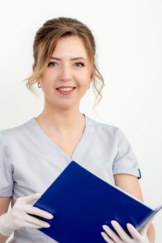 Portrait of nice young caucasian female doctor in gloves holding blue folder looking at camera on white background