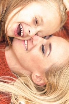 Little girl and young caucasian mom lying down directly above looking at camera on autumn leaves