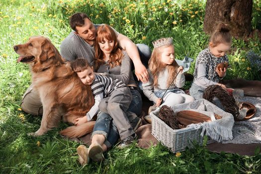 Friendly, cheerful family on a picnic with a dog lying on the grass