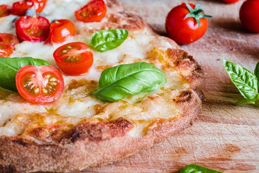 vegetarian pizza with addition of cheese, fresh tomatoes, basil on a wooden rustic table.