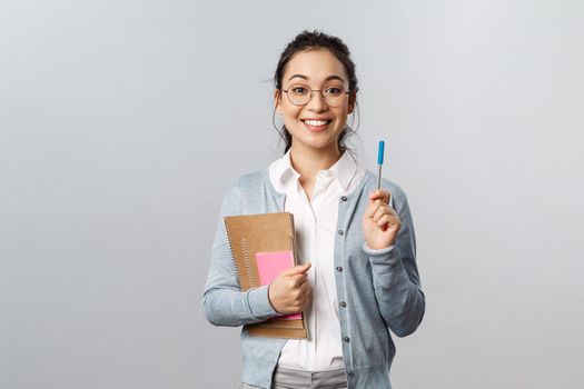Education, teachers, university and schools concept. Cute nerdy asian girl adding point, have solution to equation, raising pen to say her thought smiling, carry books and notebooks studying.