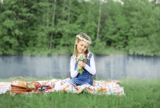 cute little girl in a wreath and a bouquet of wildflowers on a picnic in the woods on a Sunny day