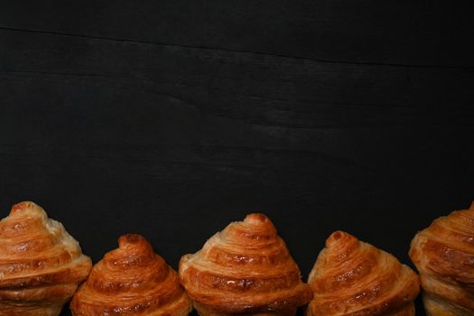 Tasty fresh croissants on black wooden background. Levitation, bread bakery products cafe concept.