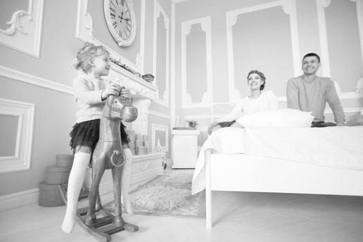little girl playing with a wooden horse in the bedroom of the parents