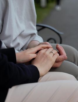 people, holidays, engagement and love concept - close up of engaged couple holding hands with diamond ring over holidays lights background