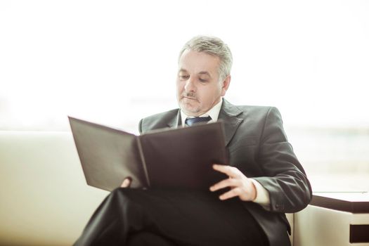 experienced businessman studies working papers sitting on a white sofa in a private office