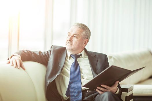 successful businessman with business documents sitting on a sofa in a private office