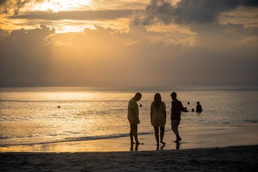 silhouette of of trio of people standing around enjoying during sunset dusk at radhasagar beach with the waves coming on the shore in havelock andaman india