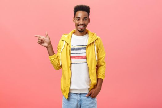 Friendly helpful male dark-skinned friend showing girlfriend appartment pointing left at living room smiling joyfully hanging out in funny and amusing company over pink background. Emotions and directions concept