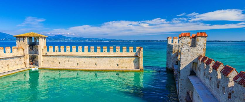 Sirmione, Italy, September 11, 2019: Small fortified harbor with turquoise water, Scaligero Castle Castello fortress, town on Garda lake, medieval castle with stone towers and brick walls, Lombardy
