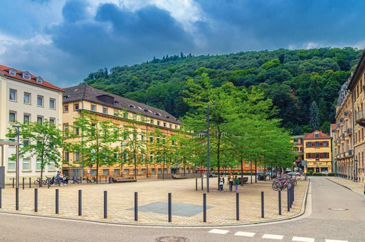 Heidelberg, Germany, August 12, 2017: Friedrich-Ebert-Platz square with buildings in Heidelberg Old town historical centre, green wooden hill background, Baden-Wurttemberg state