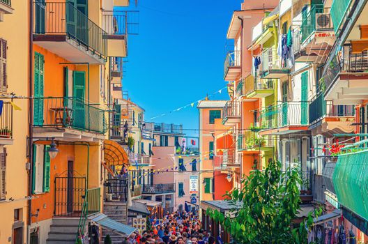 Manarola, Italy, September 12, 2018: colorful houses with flags rows, balconies, shutter windows and people tourists walking down narrow street of typical village of National park Cinque Terre