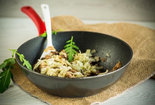 Homemade boiled noodles with meat and eggplant in a frying pan on a wooden table