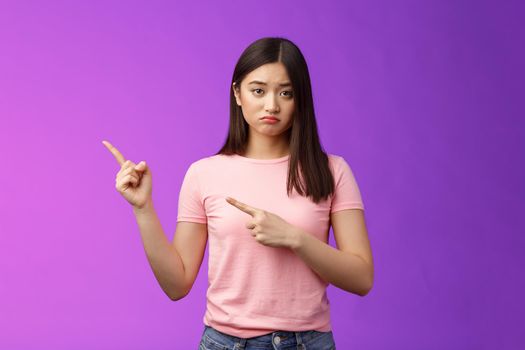 Moody upset whining girlfriend unhappy pointing left, sulking look miserable and distressed, express regret and disappointment, complain bad fortune, stand purple background displeased.