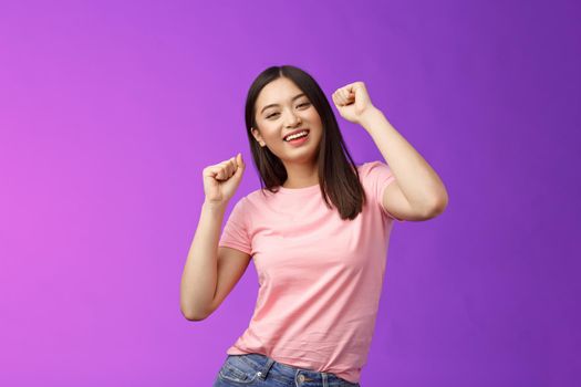 Joyful glamour asian attractive girl having fun enjoy awesome party feeling carefree, fist pump during dance, smiling broadly like good music, attend concert, stand purple background. Copy space