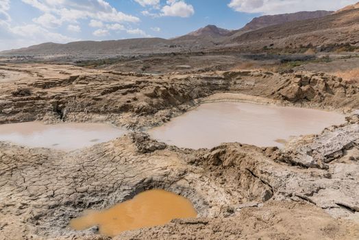 Sinkhole filled with water in different colors, near Dead Sea coastline. Hole formed when underground salt is dissolved by freshwater intrusion, due to continuing sea-level drop. . High quality photo