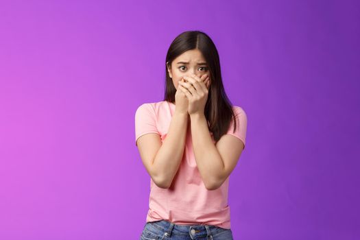 Shocked female asian victim frightened, gasping witness crime, close mouth hands, frowning, stare camera scared upset, make innocent terrified gaze, stand purple background. Copy space